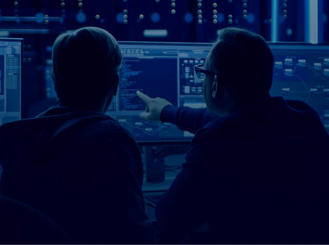 Image of two men looking at computer screen together in control room.
