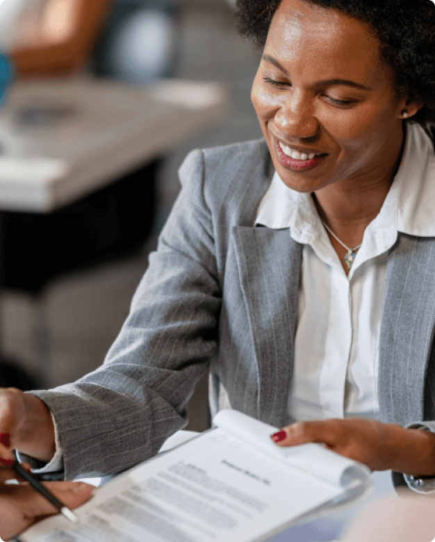 Image of woman holding a clipboard in one hand and a pen in the other. She is going through a document on the clipboard with another person who has their hand on the bottom of the clipboard.